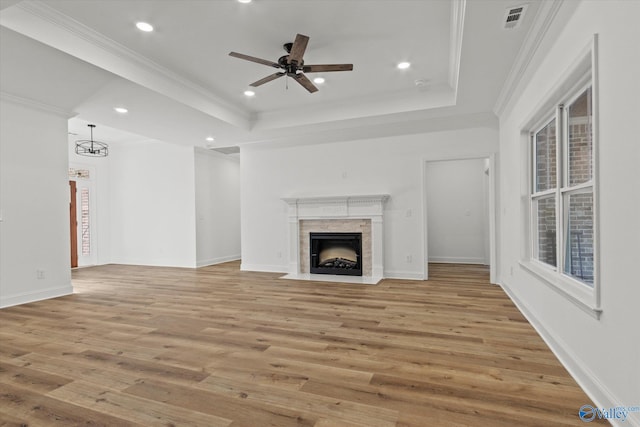 unfurnished living room with a tray ceiling, ornamental molding, ceiling fan with notable chandelier, and light wood-type flooring