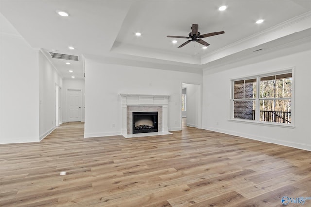 unfurnished living room with a tray ceiling, ceiling fan, crown molding, light hardwood / wood-style flooring, and a tiled fireplace