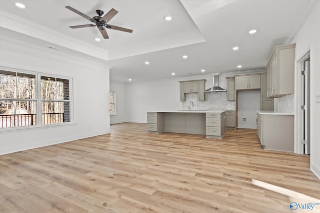 kitchen with backsplash, gray cabinetry, a tray ceiling, wall chimney range hood, and light hardwood / wood-style floors