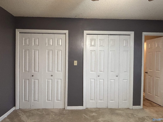 unfurnished bedroom with multiple closets, carpet, a textured ceiling, and baseboards