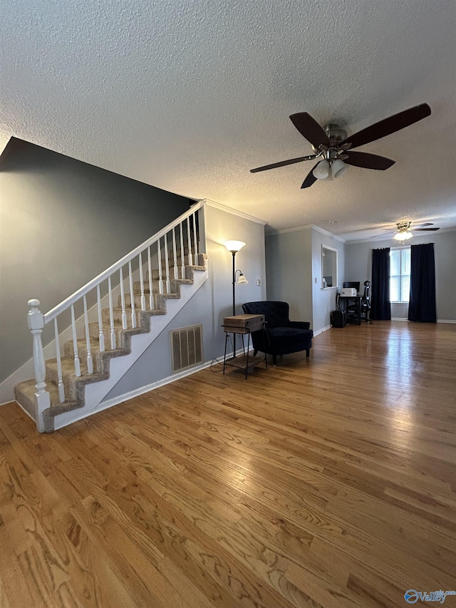 interior space with visible vents, ceiling fan, stairway, wood finished floors, and crown molding