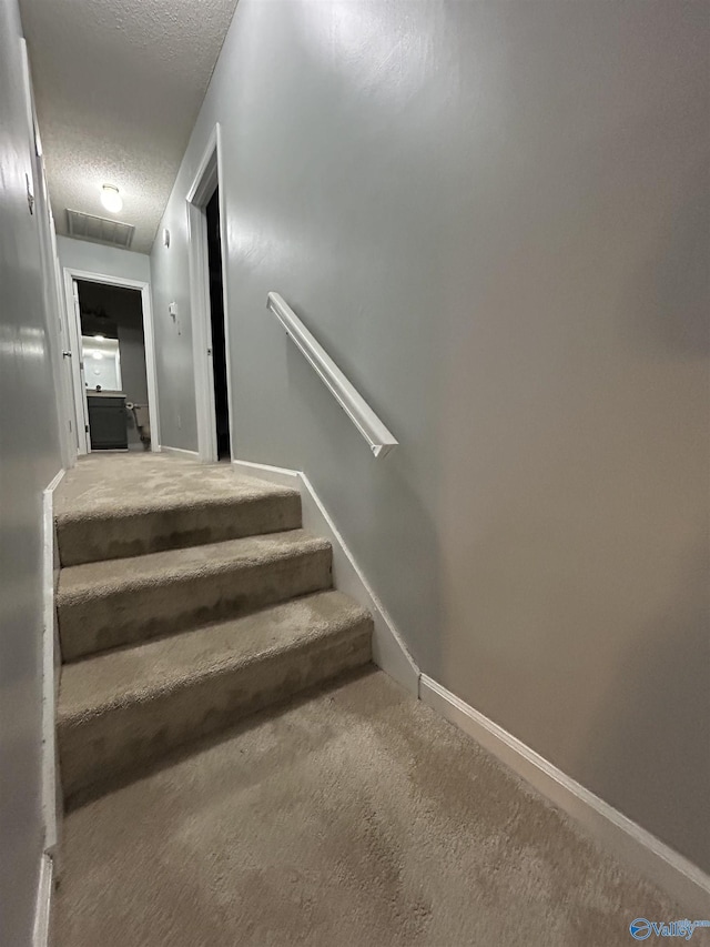 stairway with visible vents, carpet flooring, a textured ceiling, and baseboards