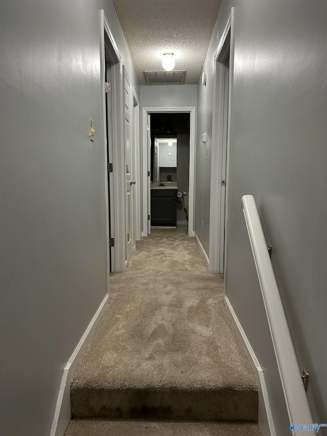 hall with light carpet, a textured ceiling, visible vents, and baseboards