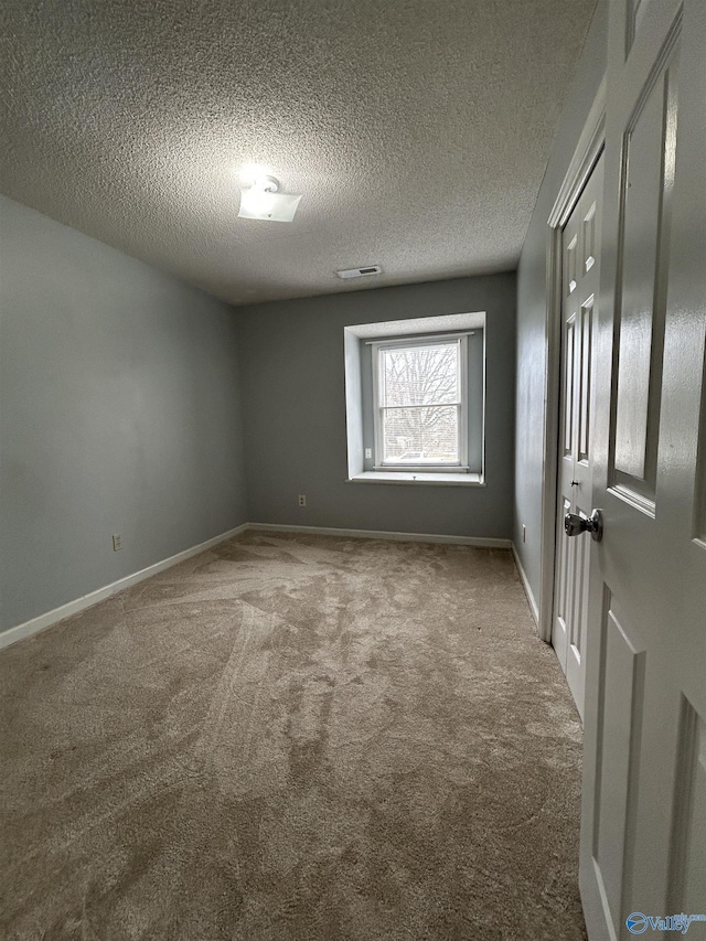 carpeted spare room featuring visible vents, baseboards, and a textured ceiling