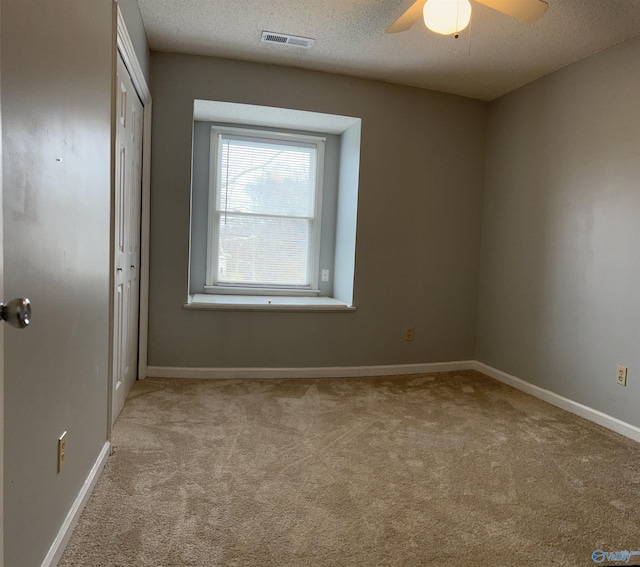 carpeted empty room with a textured ceiling, a ceiling fan, visible vents, and baseboards