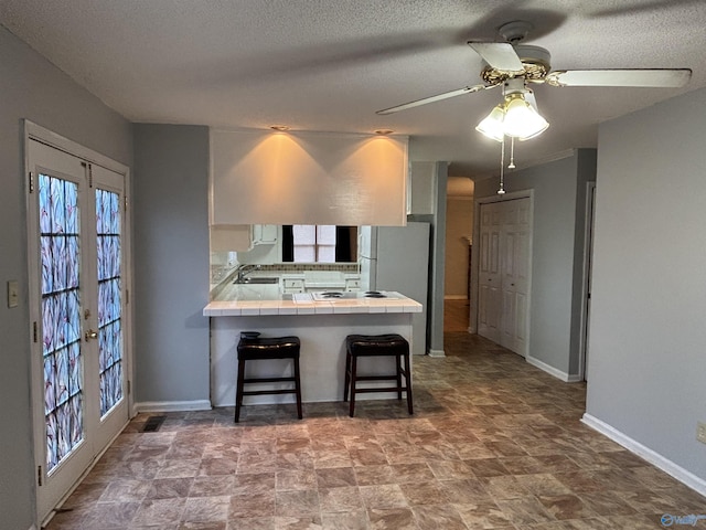 kitchen with a breakfast bar, tile counters, freestanding refrigerator, a sink, and a peninsula