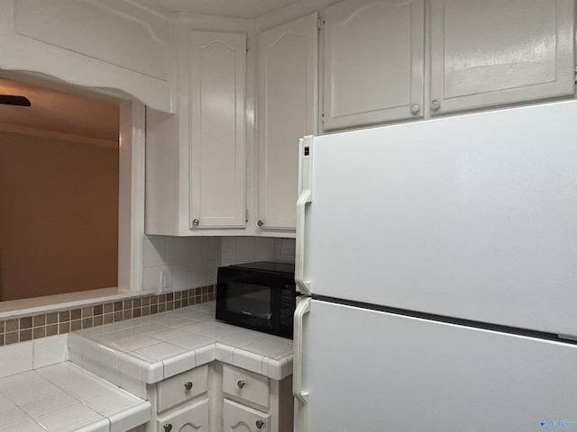 kitchen featuring black microwave, tile countertops, backsplash, and freestanding refrigerator