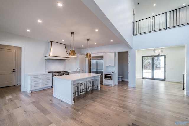 kitchen featuring appliances with stainless steel finishes, a kitchen breakfast bar, premium range hood, decorative light fixtures, and an island with sink