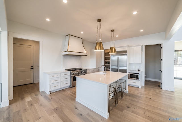 kitchen featuring custom range hood, premium appliances, a center island with sink, light hardwood / wood-style flooring, and white cabinetry