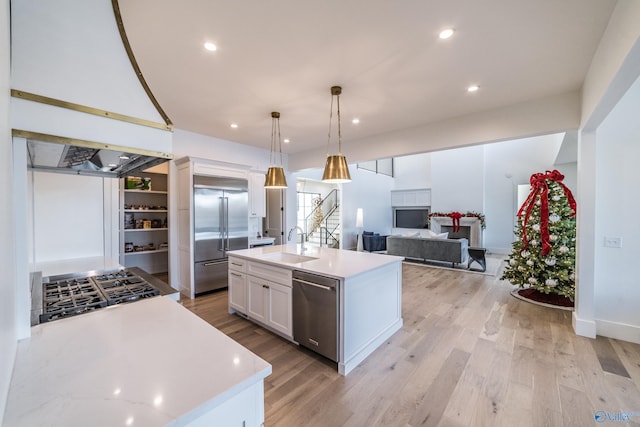 kitchen with an island with sink, pendant lighting, light hardwood / wood-style floors, white cabinets, and appliances with stainless steel finishes