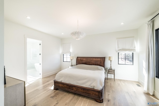 bedroom featuring ensuite bath, light hardwood / wood-style floors, multiple windows, and a notable chandelier