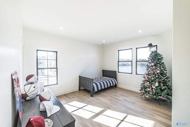 bedroom with a water view, light hardwood / wood-style flooring, and multiple windows