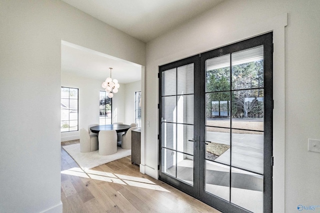 doorway featuring a healthy amount of sunlight, light hardwood / wood-style floors, french doors, and a chandelier