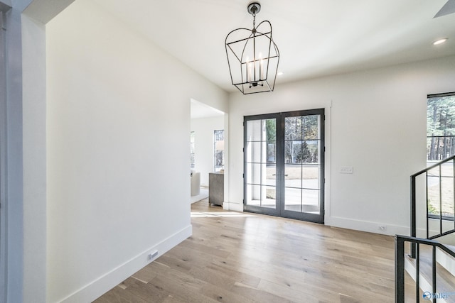 interior space with french doors, an inviting chandelier, a healthy amount of sunlight, and light hardwood / wood-style flooring