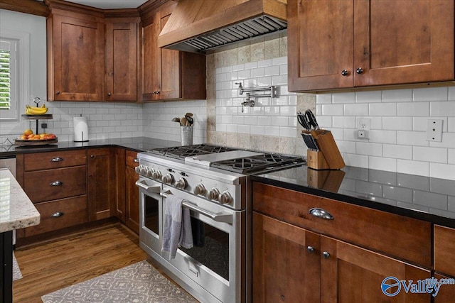 kitchen featuring custom exhaust hood, dark wood-type flooring, range with two ovens, dark stone countertops, and backsplash