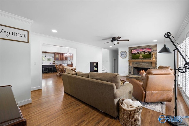 living room featuring ornamental molding, wood finished floors, a fireplace, stairway, and ceiling fan with notable chandelier