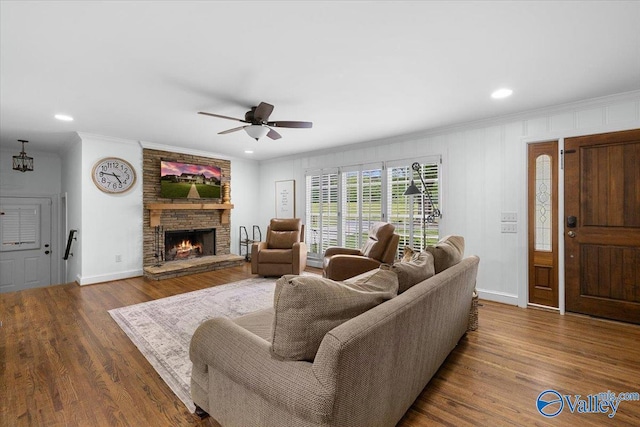 living room featuring crown molding, a stone fireplace, a ceiling fan, baseboards, and wood finished floors