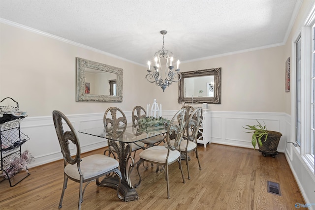dining space with a chandelier, wood finished floors, a wainscoted wall, ornamental molding, and a textured ceiling