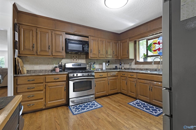 kitchen with stainless steel appliances, a sink, a textured ceiling, light wood-style floors, and tasteful backsplash
