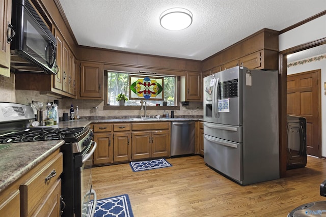 kitchen featuring stainless steel appliances, a sink, light wood-style floors, a textured ceiling, and tasteful backsplash