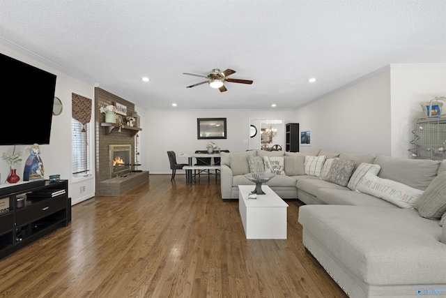 living room featuring ceiling fan, ornamental molding, a fireplace, wood finished floors, and recessed lighting