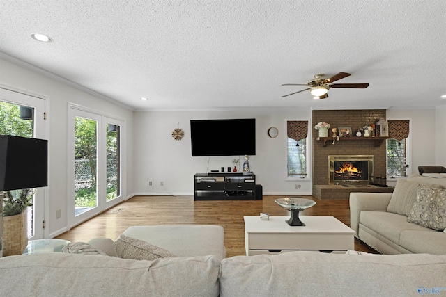 living area featuring plenty of natural light, wood finished floors, a textured ceiling, ceiling fan, and a brick fireplace