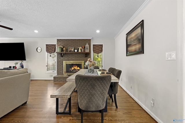dining area featuring crown molding, a textured ceiling, wood finished floors, a fireplace, and ceiling fan