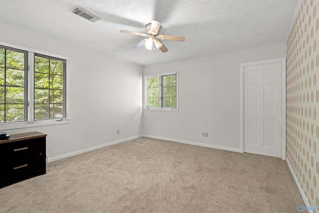 spare room with ceiling fan, light colored carpet, baseboards, a textured ceiling, and crown molding