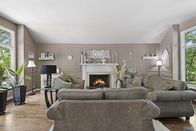 living room with a decorative wall, lofted ceiling, a lit fireplace, and wood finished floors