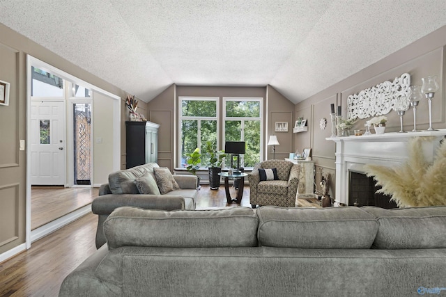 living area featuring lofted ceiling, wood finished floors, a fireplace, and a textured ceiling