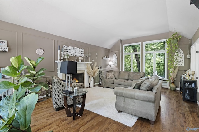 living room featuring vaulted ceiling, wood finished floors, a decorative wall, and a multi sided fireplace