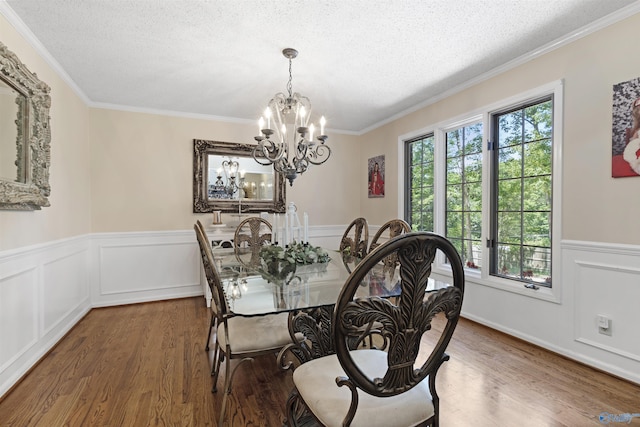 dining area featuring a textured ceiling, wood finished floors, a chandelier, a wainscoted wall, and crown molding