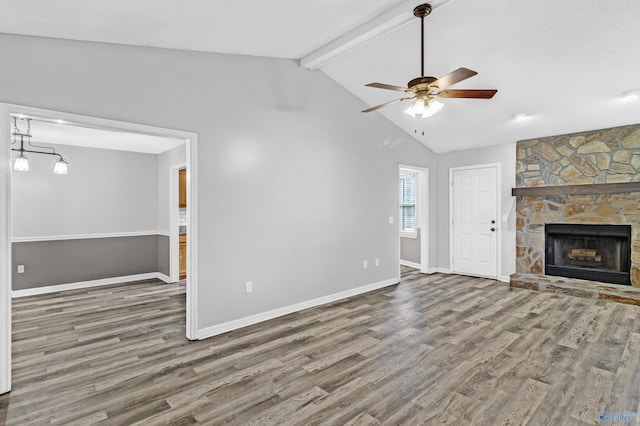 unfurnished living room with lofted ceiling with beams, ceiling fan, a stone fireplace, and wood-type flooring