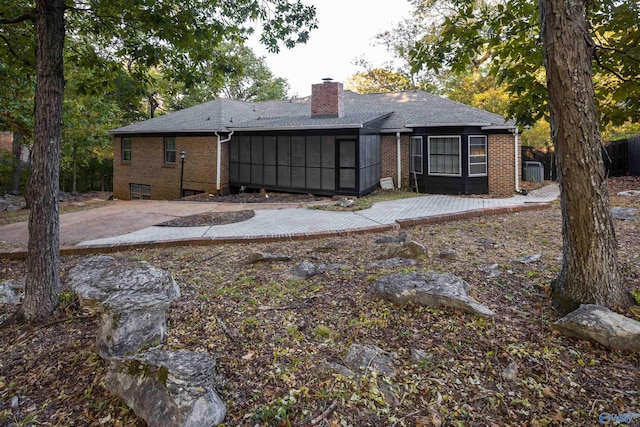 back of house with central air condition unit, a sunroom, brick siding, a chimney, and a patio area