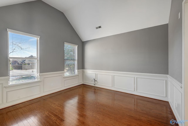 unfurnished room with a wainscoted wall, visible vents, vaulted ceiling, and wood finished floors