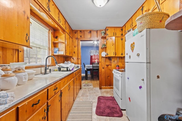 kitchen featuring light countertops, brown cabinetry, a sink, wood walls, and white appliances