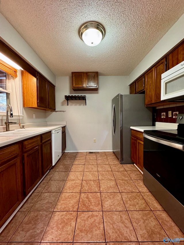 kitchen featuring light tile patterned floors, stainless steel appliances, light countertops, a sink, and a textured ceiling