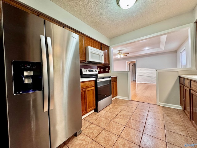 kitchen with light tile patterned floors, stainless steel appliances, light countertops, decorative backsplash, and brown cabinetry