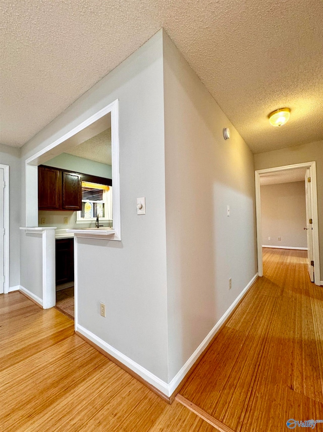 hall with baseboards, a textured ceiling, and light wood-style floors