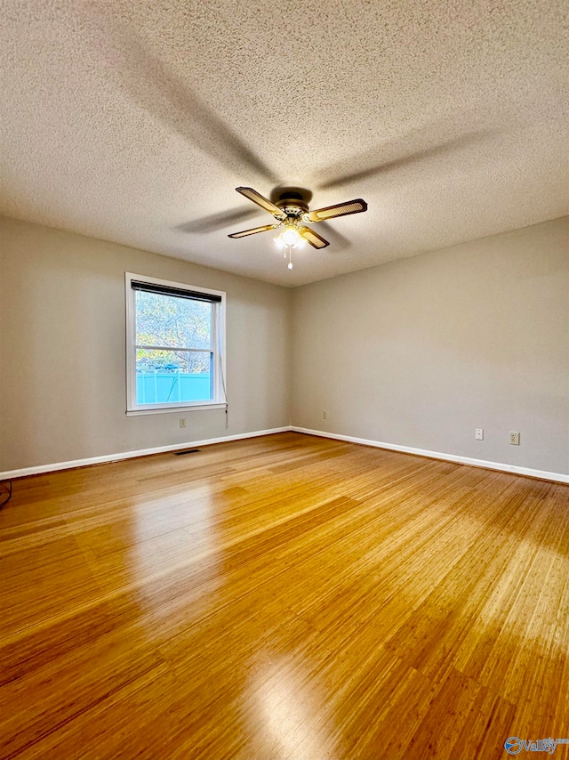 empty room with a ceiling fan, wood finished floors, visible vents, and baseboards