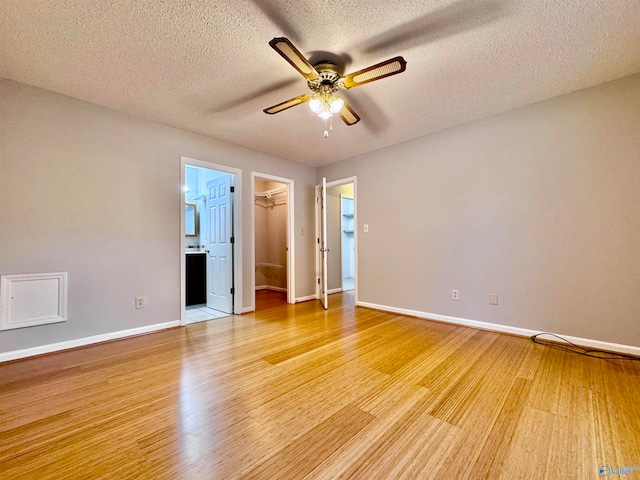 spare room featuring light wood-type flooring, a textured ceiling, baseboards, and a ceiling fan