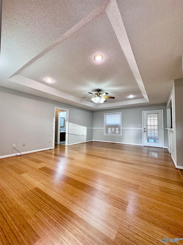 unfurnished living room with baseboards, a raised ceiling, a ceiling fan, wood finished floors, and a textured ceiling