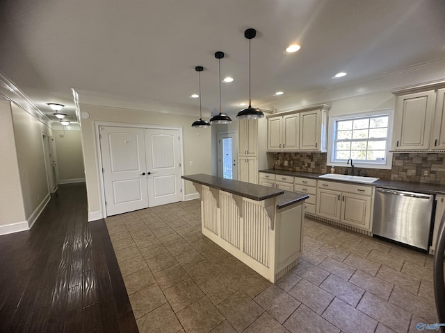 kitchen with stainless steel dishwasher, dark countertops, a kitchen bar, cream cabinets, and a sink