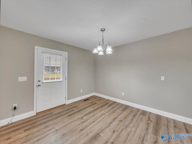 unfurnished dining area featuring baseboards, wood finished floors, and an inviting chandelier