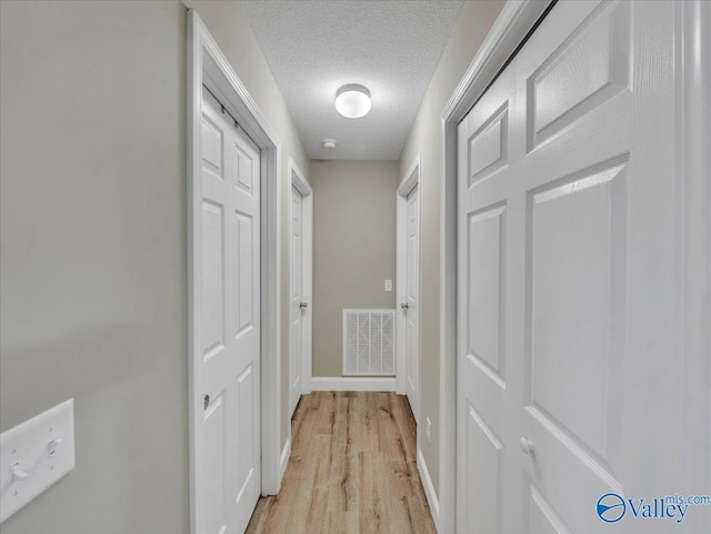 corridor with baseboards, visible vents, a textured ceiling, and light wood-style flooring