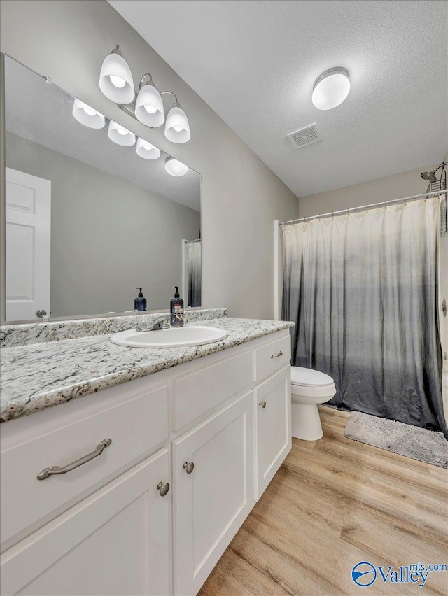 full bath featuring wood finished floors, toilet, vanity, visible vents, and a textured ceiling