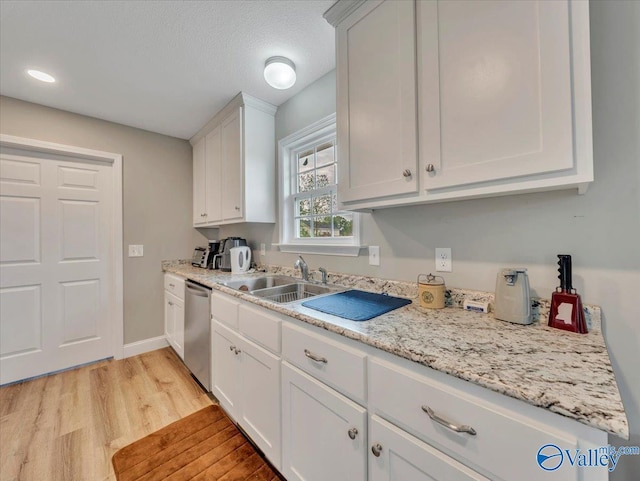 kitchen featuring a sink, light wood-style floors, baseboards, dishwasher, and white cabinets