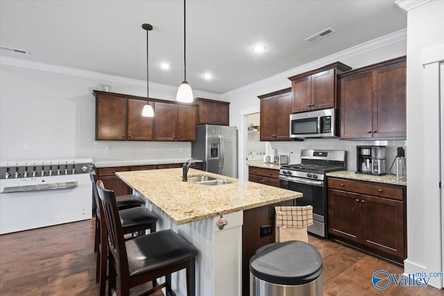 kitchen with visible vents, hanging light fixtures, appliances with stainless steel finishes, a kitchen island with sink, and a sink