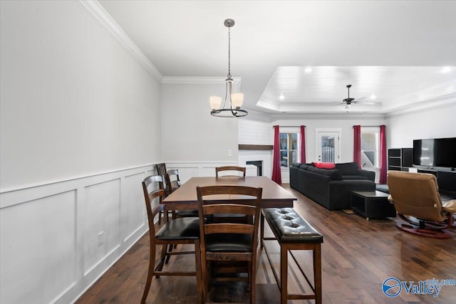 dining room featuring a wainscoted wall, dark wood finished floors, a brick fireplace, a raised ceiling, and crown molding