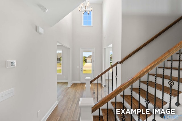 entrance foyer featuring light wood-type flooring, a towering ceiling, and an inviting chandelier